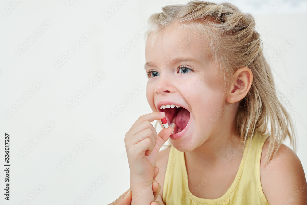 Positive pretty blond little girl taking pill of supplement, vitamin or medicine Positive pretty blond little girl taking pill of supplement, vitamin or medicine