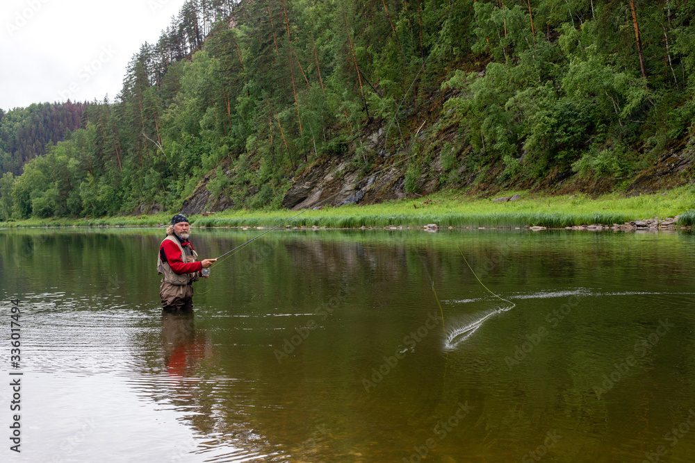 elderly fisherman alone stand in river water. Man bearded with fishing rod in fishing equipment. Hobby sport activity
