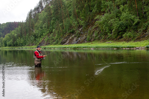 elderly fisherman alone stand in river water. Man bearded with fishing rod in fishing equipment. Hobby sport activity