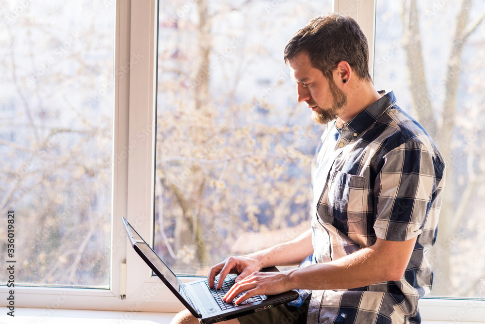 Fototapeta premium Business man working on a laptop while sitting on a windowsill.