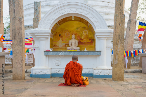 Canvas Print Buddhist monk meditates at Buddha sculpture