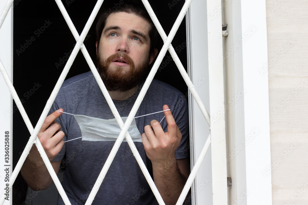male model in a disposable mask, dark hair, beard and grey t-shirt.A coronavirus patient remains at home under quarantine and disease prevention.Sad and negative Emotions in the eyes of a person male model in a disposable mask, dark hair, beard and grey t-shirt.A coronavirus patient remains at home under quarantine and disease prevention.Sad and negative Emotions in the eyes of a person