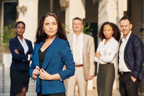 Portrait of young serious businesswoman standing outdoors in front of her colleagues