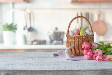 Easter composition with bunny and colorful eggs in basket, bouquet tulip on kitchen wooden table. Spring decor with space for text.