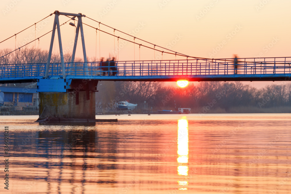 Obraz premium A suspension footbridge with motion blurred people silhouettes at the sunrise