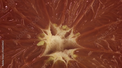 Extreme close up cinematic footage of rotating grapefruit on table. Red fruit spin around its axis.