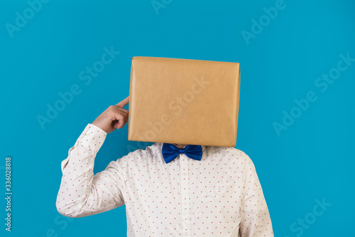 Hombre con caja de cartón en la cabeza con gesto pensativo y dedo de la mano apuntando a su cabeza, gesto actitud pensativo idea sobre fondo azul clásico. Vista de frente. Copy space