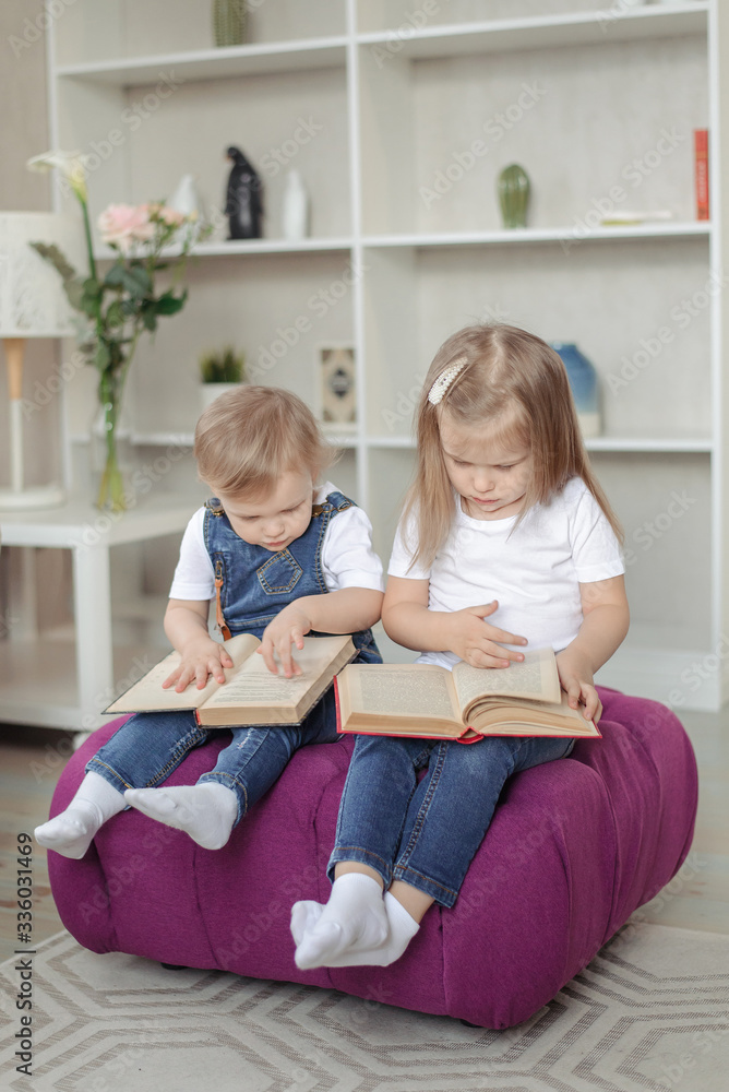 Two girl daughters sit on a chair at home and learn to read books. Distance learning of the school during quarantine. Two girl daughters sit on a chair at home and learn to read books. Distance learning of the school during quarantine.