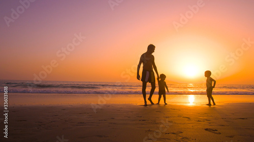 Father with kids playing in the beach at sunset