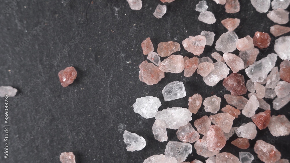 Fototapeta premium Beautiful macro shot footage close up Himalayan salt lies on a black stone. Crystals of various breeds, pink, white - lie on a fossil.