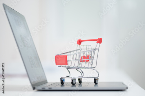 Red trolley on laptop keyboard.A cart and notebook computer on white background.Electronic commerce that allows consumers to directly buy goods from a seller over the internet.Shopping online concept.