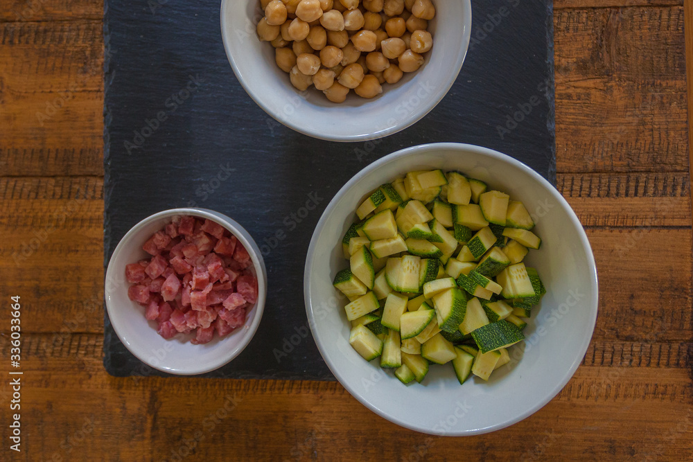 Top view of cups full of zucchini, bacon and chickpeas over a slate plate and wooden background. Concept: food porn dinner, food lovers, restaurant Top view of cups full of zucchini, bacon and chickpeas over a slate plate and wooden background. Concept: food porn dinner, food lovers, restaurant