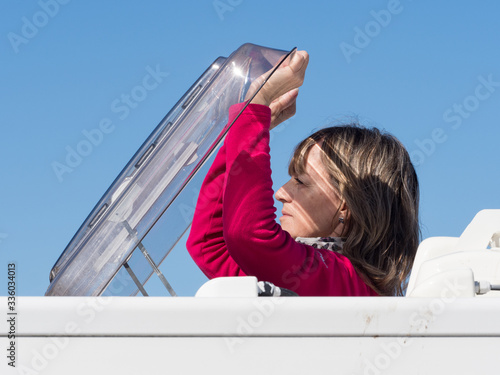 A lady motorhome owner's head and arms can be seen as she has climbed through the roof of her recreational vehicle and opens the skylight hatch.Image photo