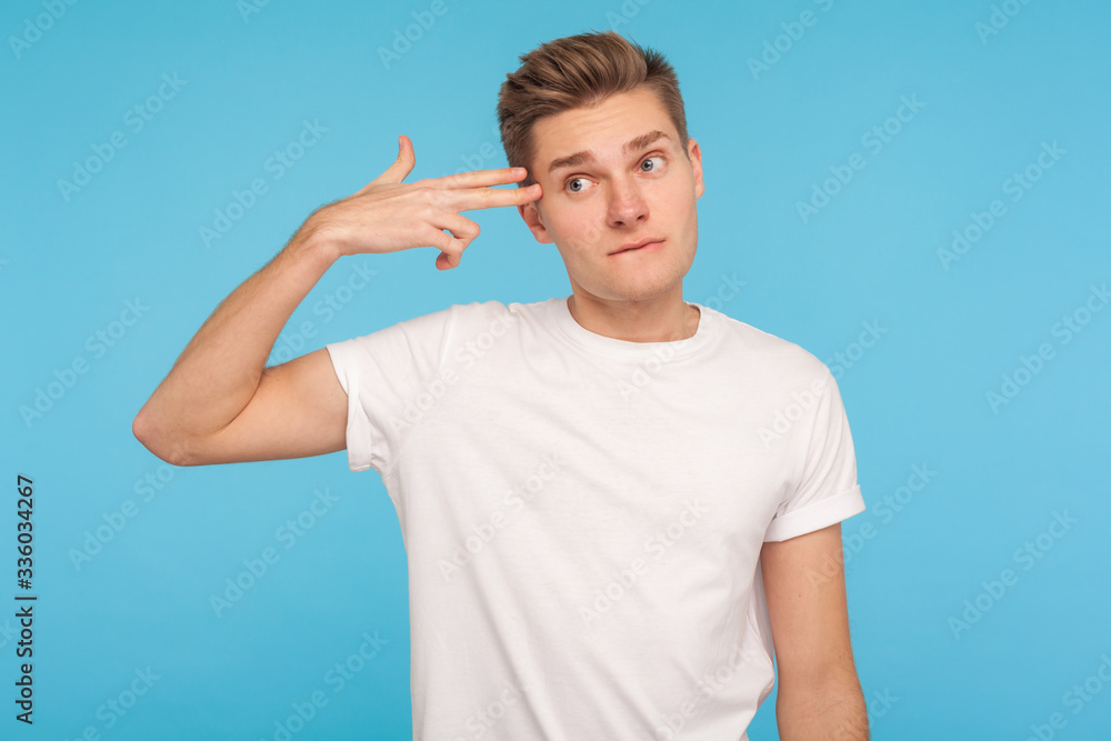 Suicide gesture. Portrait of depressed unhappy man in t-shirt pointing finger gun to head and looking with tedious indifferent expression, bored of life. indoor studio shot isolated on blue background Suicide gesture. Portrait of depressed unhappy man in t-shirt pointing finger gun to head and looking with tedious indifferent expression, bored of life. indoor studio shot isolated on blue background