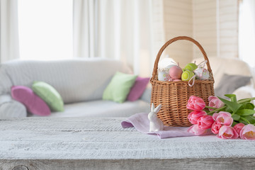 Easter composition with bunny and eggs in basket, tulips on wooden table. Spring home cozy interior. Space for design.