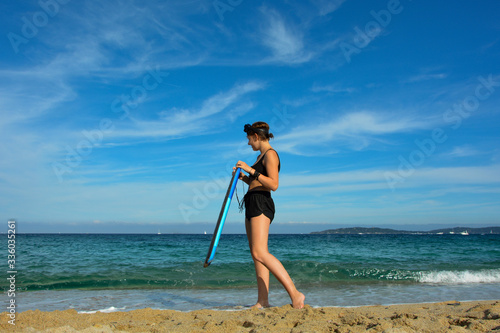 Fototapeta Naklejka Na Ścianę i Meble -  Young girl stands with a swimming board on the beach, the coast of the French Riviera in the background