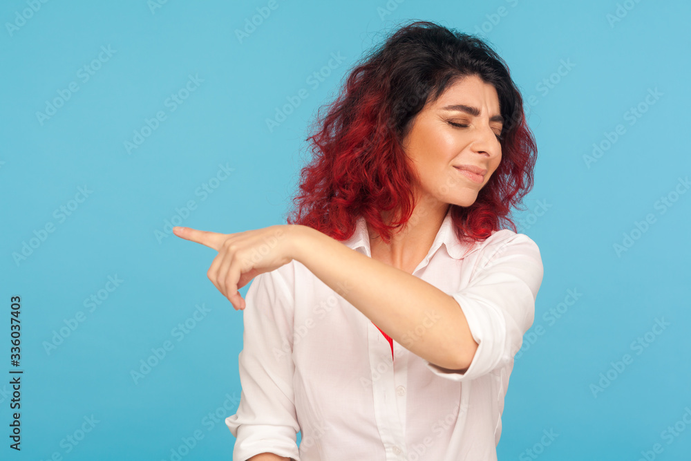Get out! Portrait of irritated girl with fancy red hair turning face with displeased annoyed expression, pointing away to kick out of home, breakup in relations. indoor studio shot, blue background Get out! Portrait of irritated girl with fancy red hair turning face with displeased annoyed expression, pointing away to kick out of home, breakup in relations. indoor studio shot, blue background