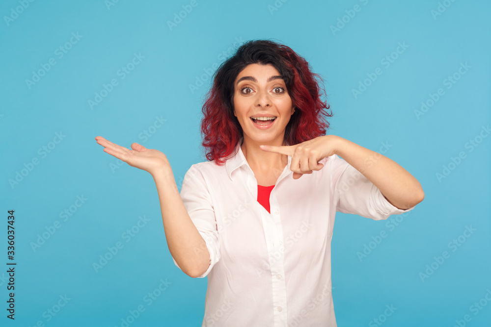 Φωτογραφία Surprised hipster woman with fancy red hair presenting advertising area on her palm and looking with amazement, showing empty space for awesome commercial product