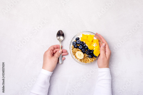 Female Hand are Holding Glass Bowl with Healthy Food Bowls of Muesl and Yogurt with Berry and Mango Top View photo