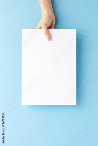 Young woman’s hand holding blank paper sheet on blue background. Mockup