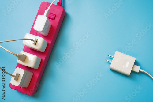 White mobile charger plugs full occupied on pink extension power strip and one plug left await in queue on blue PVC texture background ,enery management for limited resource concept photo