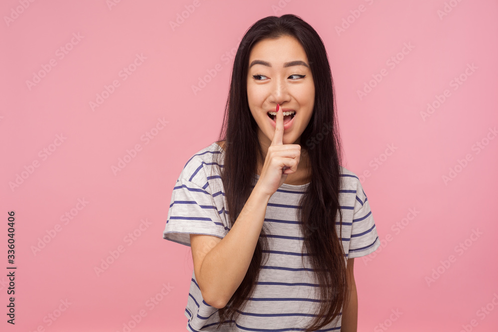 Be quiet! Portrait of positive girl with long hair in striped t-shirt gesturing for being silent, showing hush sign with finger on lips, asking to keep secret. studio shot isolated on pink background Be quiet! Portrait of positive girl with long hair in striped t-shirt gesturing for being silent, showing hush sign with finger on lips, asking to keep secret. studio shot isolated on pink background