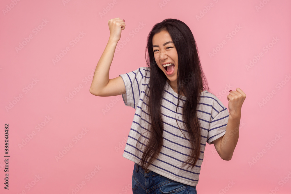 Portrait of euphoric happy joyful girl with long hair screaming with happiness and raising hands in gesture yes, hurray, I did it, celebrating victory. indoor studio shot isolated on pink background Portrait of euphoric happy joyful girl with long hair screaming with happiness and raising hands in gesture yes, hurray, I did it, celebrating victory. indoor studio shot isolated on pink background