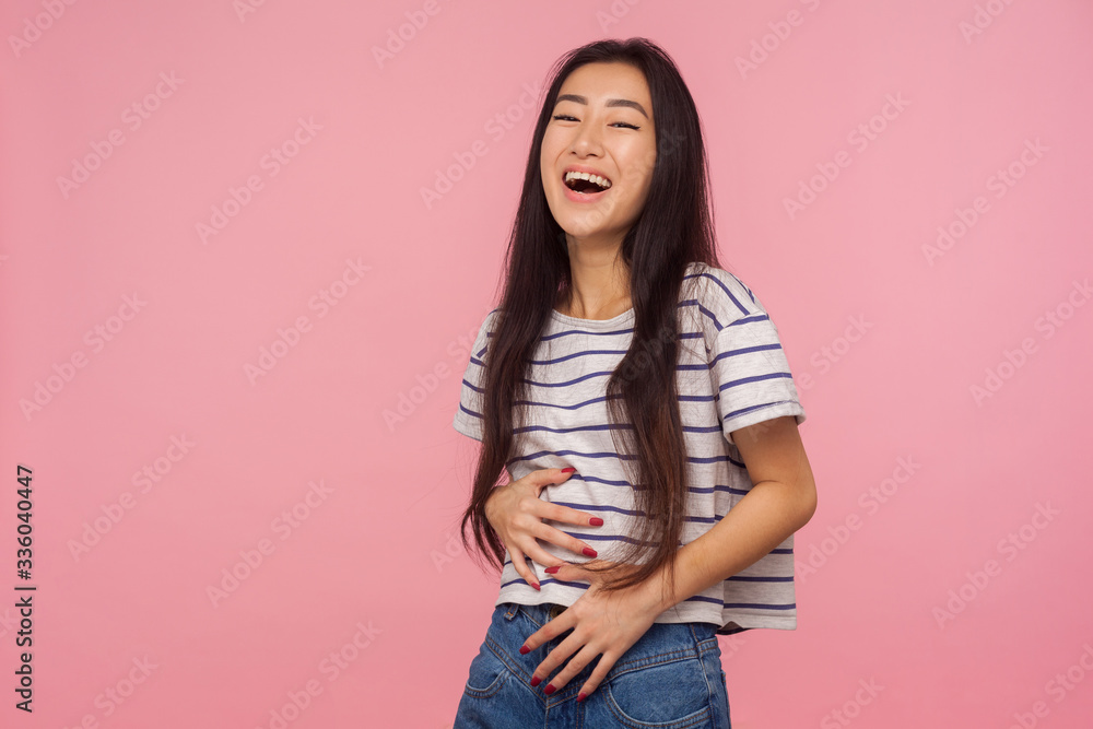 Hilarious joke! Portrait of happy optimistic girl with long hair in striped t-shirt holding belly and laughing out loud, amused by silly funny anecdote. indoor studio shot isolated on pink background Hilarious joke! Portrait of happy optimistic girl with long hair in striped t-shirt holding belly and laughing out loud, amused by silly funny anecdote. indoor studio shot isolated on pink background
