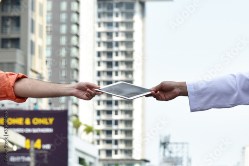 2 Men sending  4g Tablet device  in hand to hand between social distancing in Covid-19 crisis