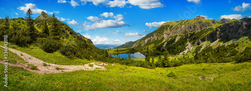Fototapeta Naklejka Na Ścianę i Meble -  Gorgeous mountain range surrounding a lake, with deep blue sunny sky and green meadows in the foreground