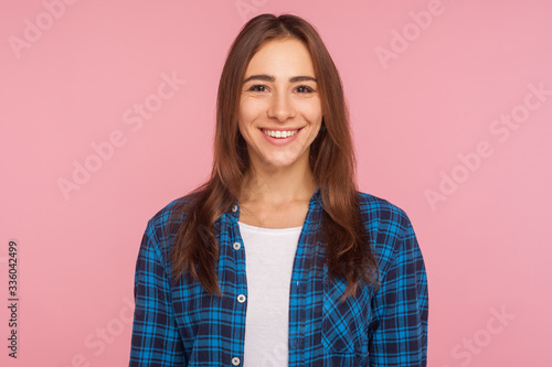 Portrait of friendly good-natured girl in checkered shirt smiling sincerely at camera, looking satisfied contented with life, rejoicing positive news. indoor studio shot isolated on pink background © khosrork