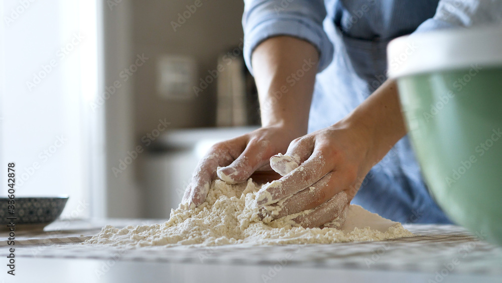Authentic close up shot of an young woman with apron is kneading a dough for pizza or pasta preparation for lunch in a kitchen. Concept of housewife, cooking, traditional italian food, authenticity