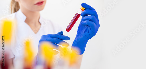 A woman's hand in a blue glove holding a blood sample in a laboratory test tube to detect viruses