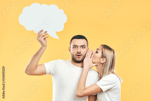 Young woman whispering secrets to man with paper thought bubble