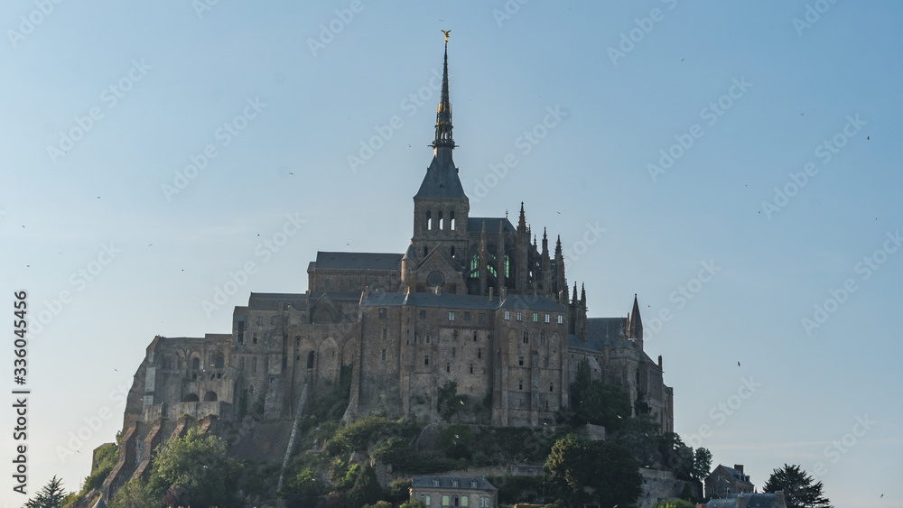 El Mont Saint Michel in France between Bretagne and Normandy, a former medieval rock abbey with vegetation and moss on the rocks, shady on the main facade.
