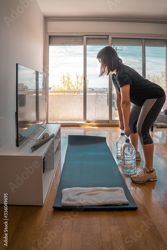 girl exercising lifting five liters water bottles in her home living room photo