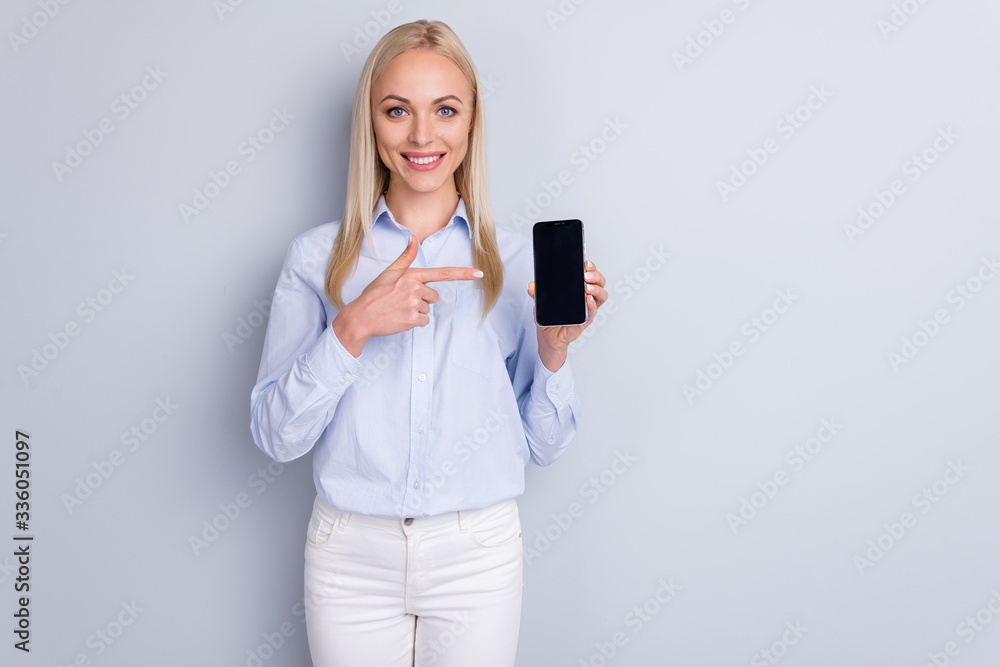 Naklejka premium Portrait of positive cheerful promoter girl hold new smartphone device point index finger suggest select wear good look trousers isolated over gray color background