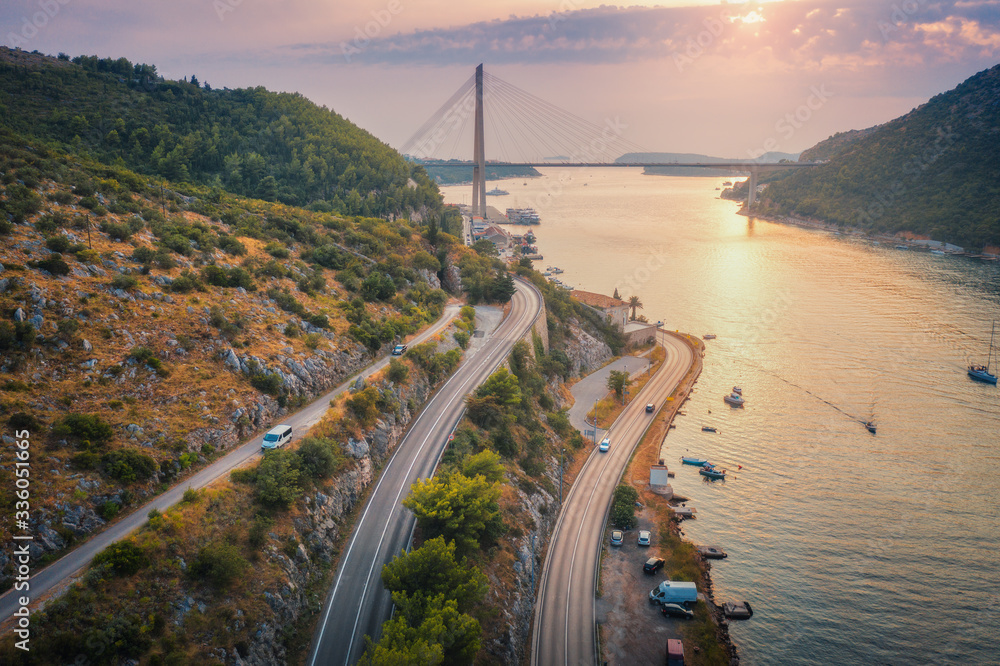 Aerial view of mountain roads  and beautiful bridge at sunset. Dubrovnik, Croatia. Top view of road, boats, yachts, green trees. Summer landscape with harbor, sea coast, highway and cloudy sky