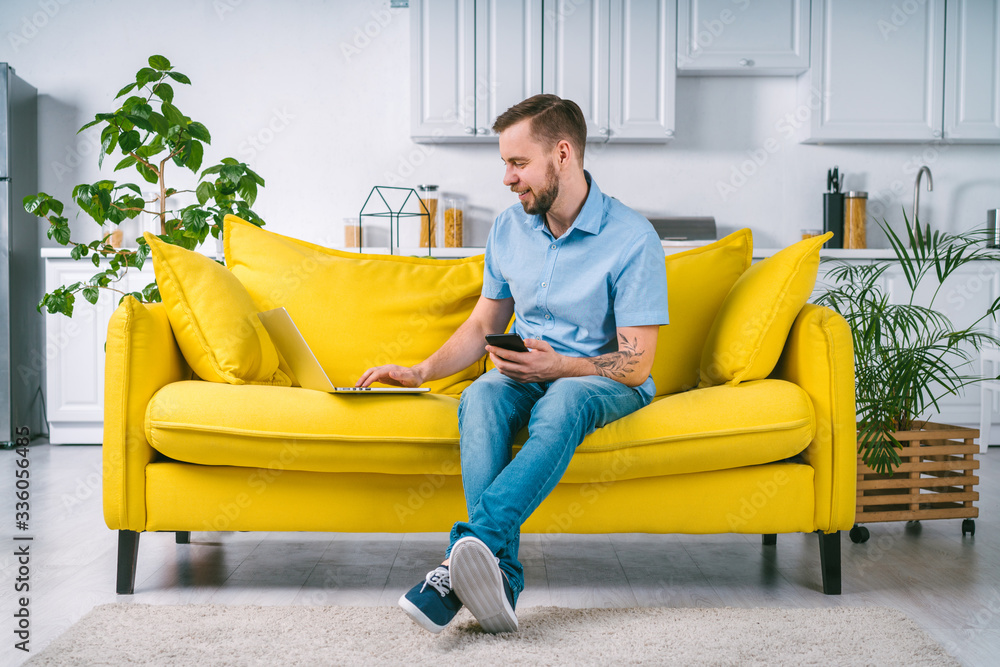 Young casually dressed male entrepreneur working distantly from home using laptop and mobile phone Young casually dressed male entrepreneur working distantly from home using laptop and mobile phone