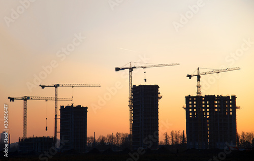 Silhouettes of tower cranes constructing a new residential building at a construction site against sunset background.