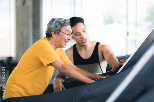 The handsome young trainer is advising the elderly to exercise using digital exercise machines in the morning exercise room. In the concept of health care for the elderly