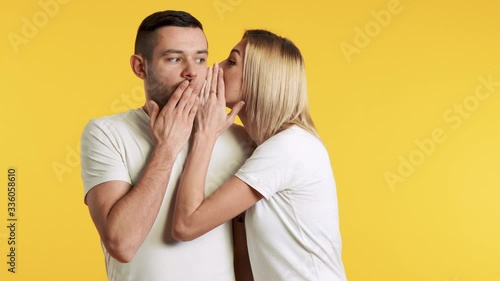 Young woman whispering secrets to surprised man over yellow background