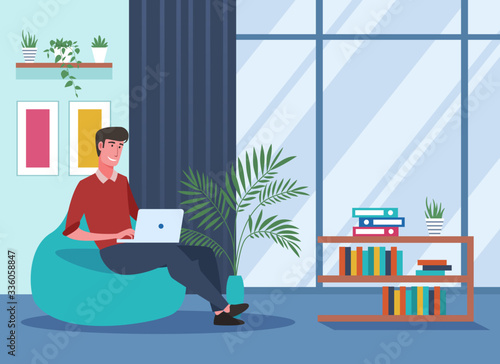 Young man working on laptop and sitting on bean bag chair at home
