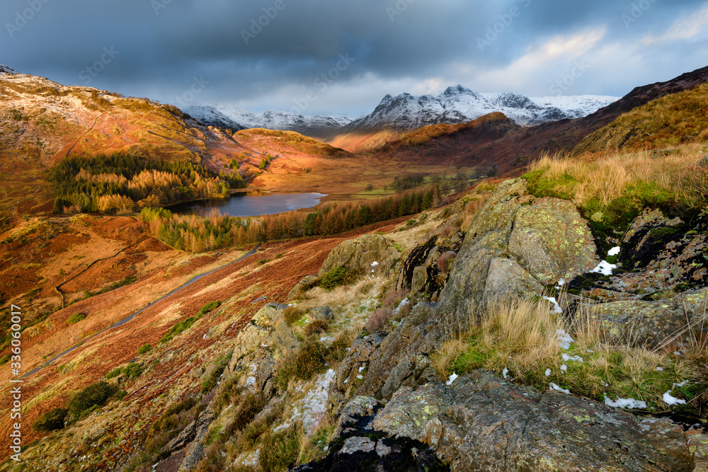Ultra Wide View Of Dramatic Landscape Blea Tarn With Snow On Langdale Pikes And Dark Moody Clouds. Lake District, UK.