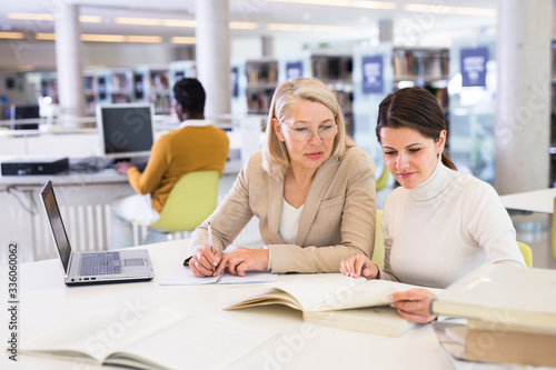 Female teacher working with girl student in university library