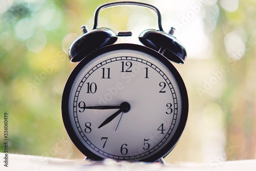 vintage alarm clock show before 8 o'clock on the table with green leafs blurred background and copy space.