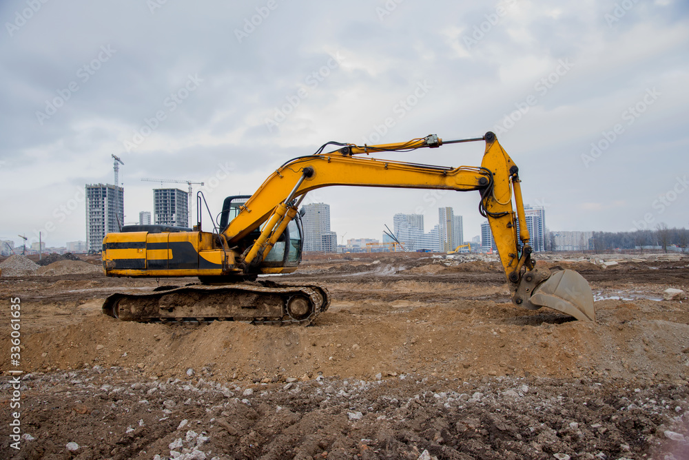 Excavators at earthworks on construction site. Backhoe loader digs a pit for the construction of the road. Digging trench for laying sewer pipes drainage in ground. Earth-Moving Heavy Equipment Excavators at earthworks on construction site. Backhoe loader digs a pit for the construction of the road. Digging trench for laying sewer pipes drainage in ground. Earth-Moving Heavy Equipment