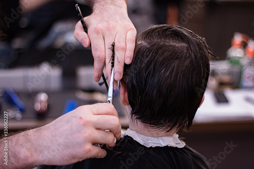 Hairdresser doing hairstyle to little boy. Barber combs little boy head.