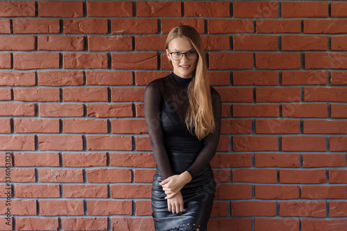 Elegant smiling woman in eyeglasses on a brick wall background