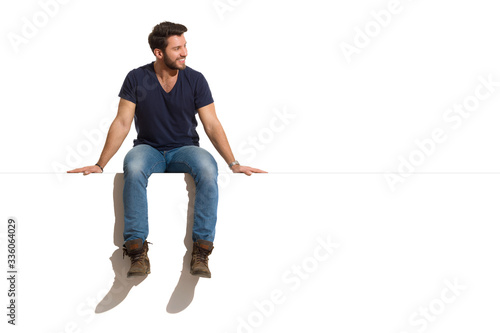 Smiling Handsome Man Is Sitting On A Top Of White Banner And Looking At The Side